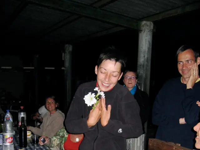A woman is standing and also laughing. Left side there are plates,food,glasses,bottles on the...