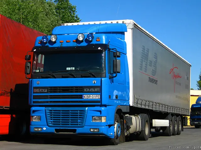 In this image I can see few blue colour trucks, a red colour thing, few trees, the sky and on this...