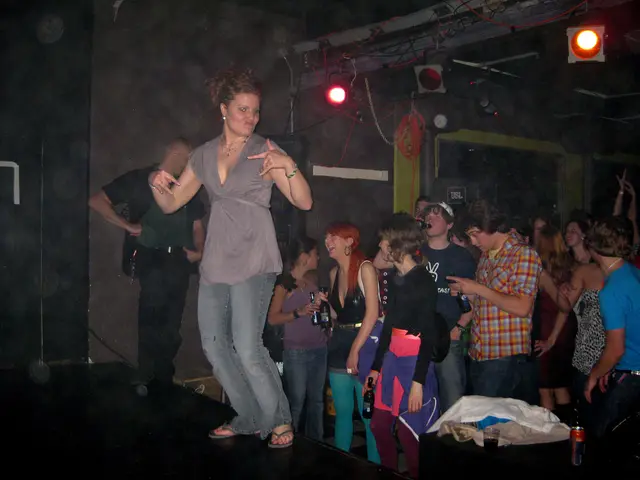 This picture shows few people standing and a man drinking beer by holding a bottle in his hand and...