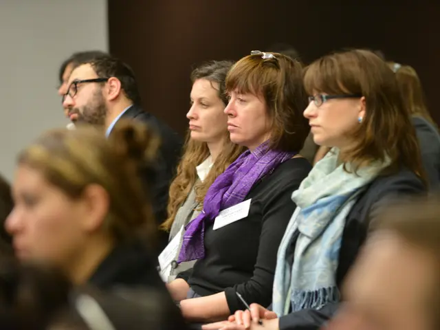 The foreground of the picture is blurred. In the center of the picture there are women sitting in...