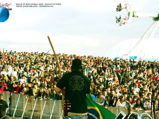 In this picture we can see a man wearing black color t-shirt standing on the stage playing guitar....