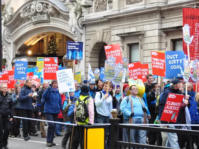 There are persons in different color dresses. Some of them are holding placards. On the right side,...