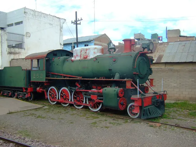 In the image there is a train in the foreground, behind the train there is a wall and in the...