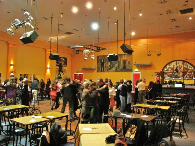 this picture shows a group of people standing and we see chairs and tables around and we see people...