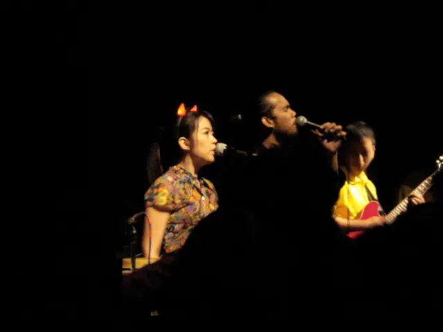 This woman and this man is singing in-front of mic. This person is playing a guitar.