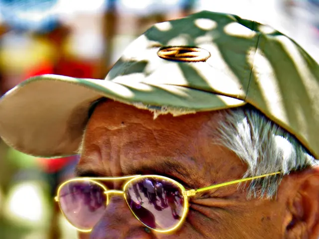 In the image there is an old man with a cap on his head. He kept goggles and he is smiling. Behind...