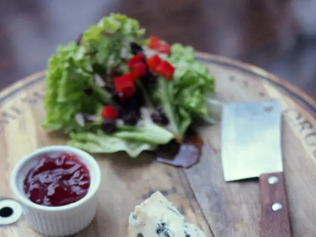 In this picture we can see a wooden chopping board, we can see leafy vegetable, a cup, a knife and...
