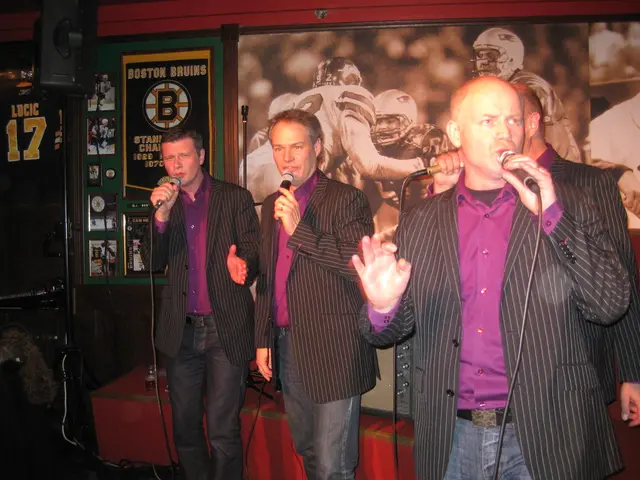 This image consists of four men wearing same dresses and holding mics. They are singing. In the...