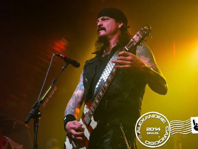 A man is standing and also playing the guitar. He wear a cap on his head there is a microphone in...