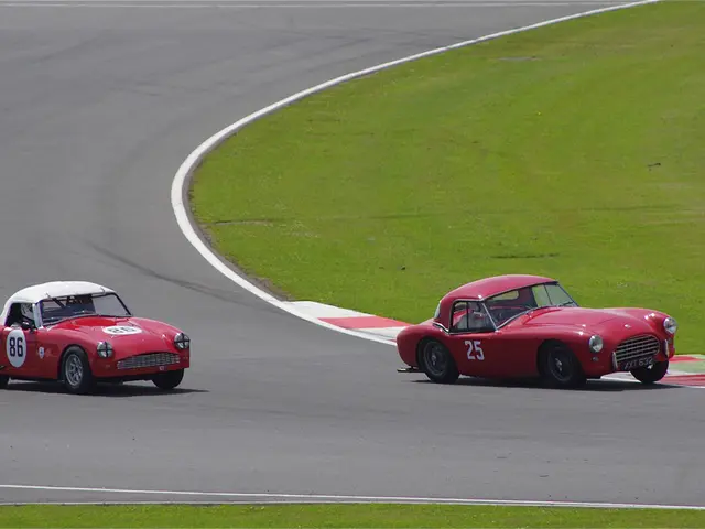 In this picture there are two red color cars, racing on the runway track. On the right side we can...