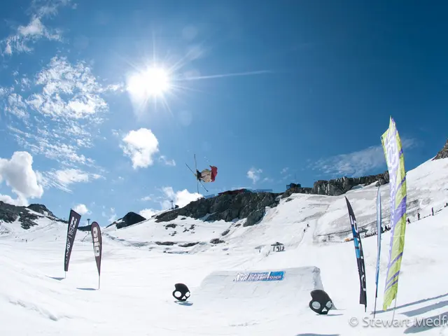 There is snow and there is a person wearing skis is in the air and there are mountains in the...