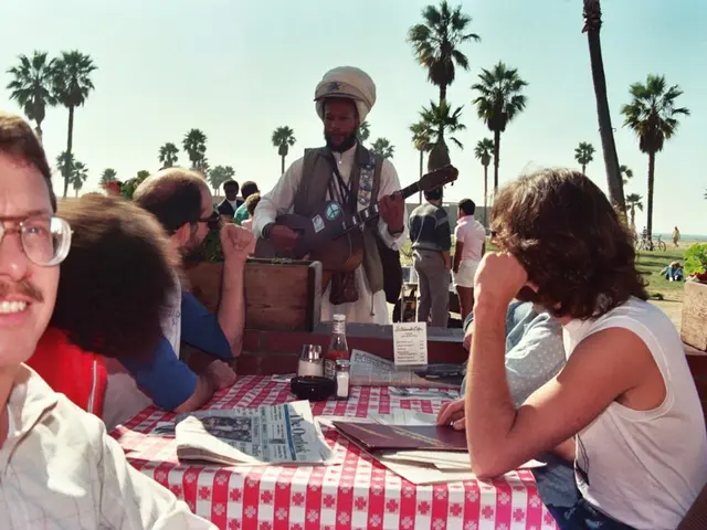 In this image I see number of people in which these 5 of them are sitting and I see a table on...