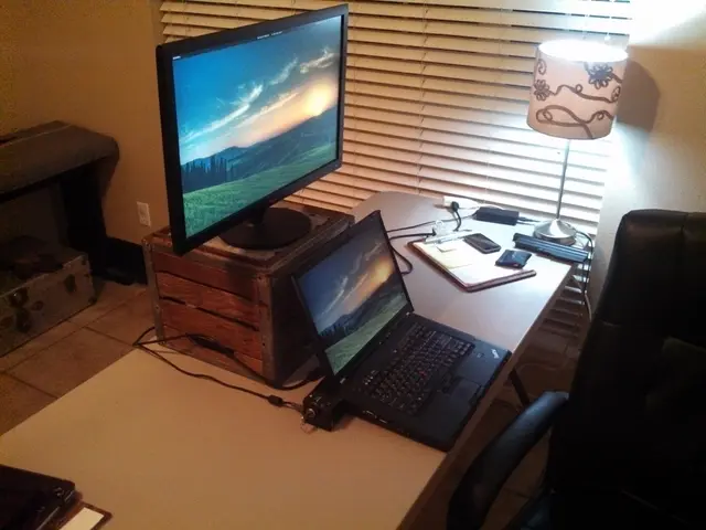 On this table there is a box, monitor, laptop, pad, papers, mobiles, lantern lamp and cable. This...