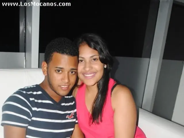 This picture shows a man and a woman seated on the sofa and we see text on the top left corner and...