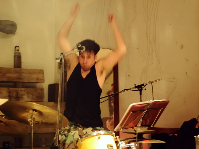 This person sitting and playing musical instrument. There is a microphone with stand. On the...