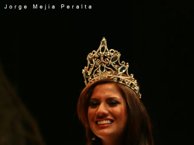 In the image there is a lady with a crown on her head. And there is a sash. And she is holding a...