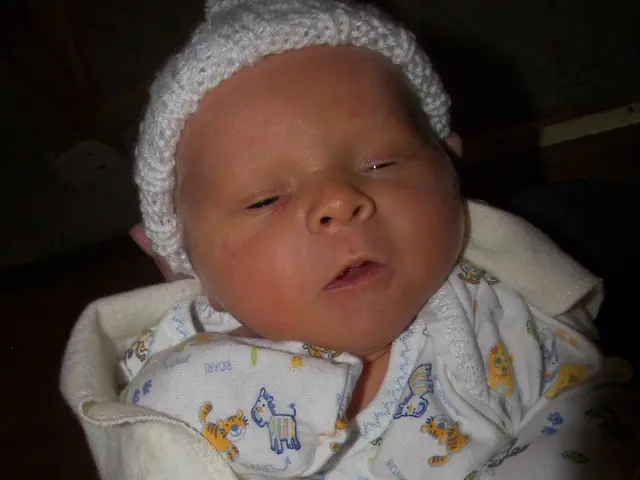 In this image I can see a baby wearing white and cream colored clothes. I can see the black colored...