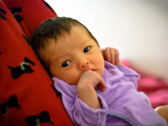 In the center of the image we can see a baby lying on some object, which is in a red and black...