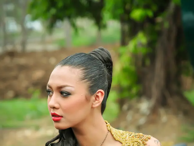 In this image we can see a lady sitting on a car and she wore a gold color dress and a star pendant...