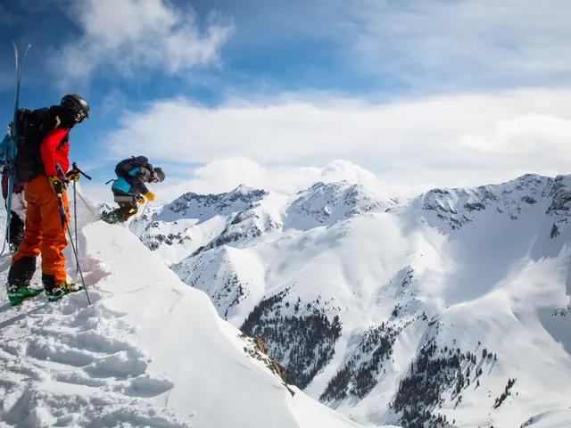 In this image I can see some snow and few persons wearing orange, black and blue colored dresses...