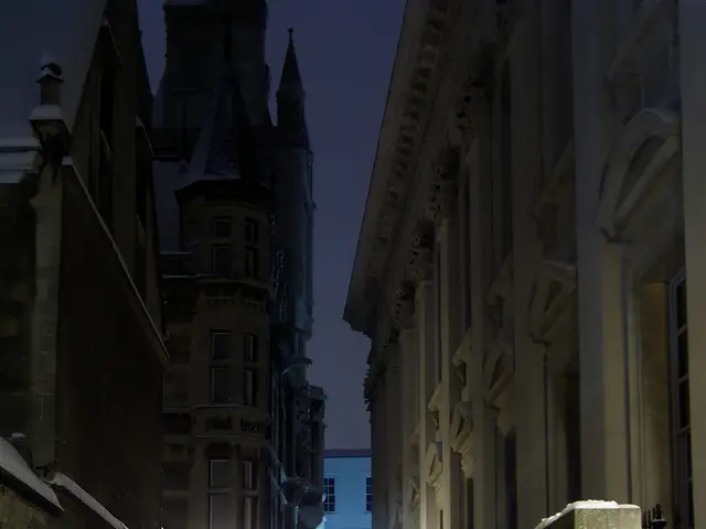 This image consists of a road on which there is snow.. To the right, there is a buildings along...