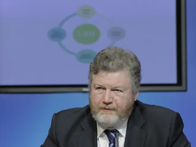 A man is present wearing a suit. There is a screen behind him.