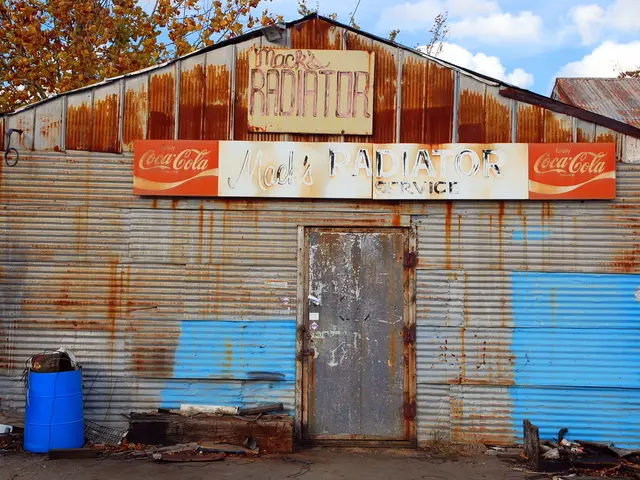In this image there is a shed which is made up of asbestos sheets. There is a hoarding to it. In...