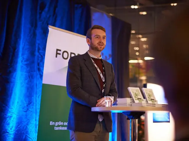 This is the picture of a man standing on a stage, in front of the man there is a table on the table...
