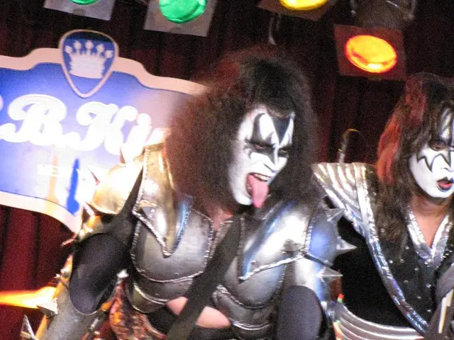 There are two persons standing and holding guitars in their hands. These people are wearing some...