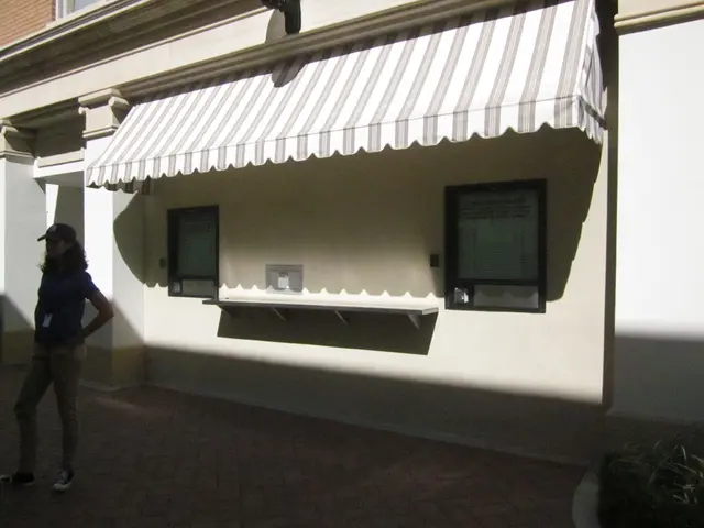 In this image we can see a woman standing and wearing a cap, behind her there is a building with...