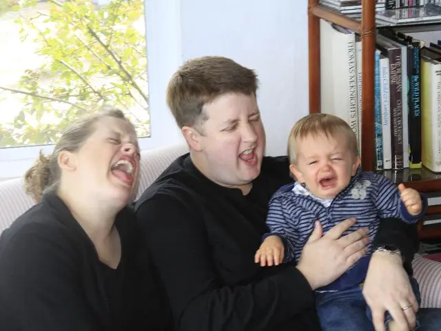 In this picture we can see there are two people sitting on a couch and a man is holding a kid and...