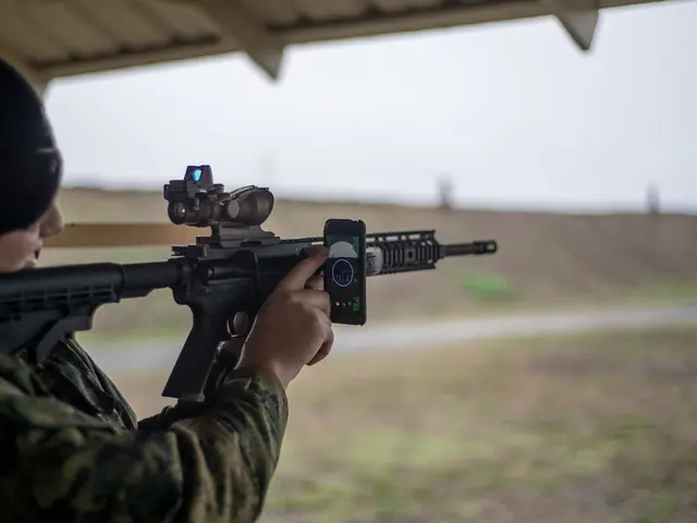 In the foreground of this picture, there is a man holding a gun in his hand and operating a mobile...