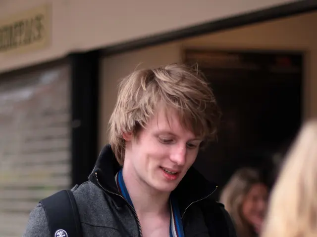 The man in the middle of the picture wearing a black jacket and black backpack is holding something...