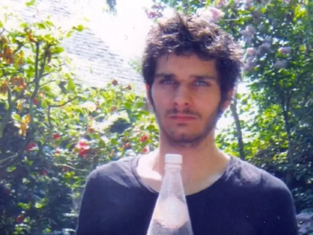 a person is standing wearing a black t shirt. he is holding a shoe in his hand. in the show there...