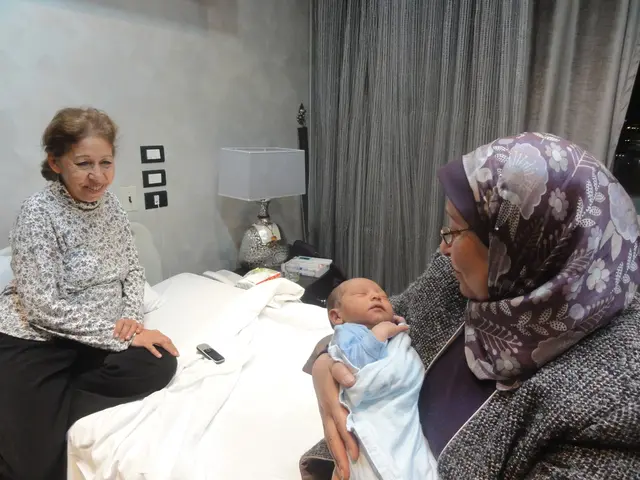 This image is clicked in a room. There are two women sitting on a bed. The woman to the left corner...