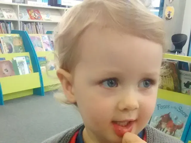In this image there is a small baby boy standing beside him there are some shelves with books.