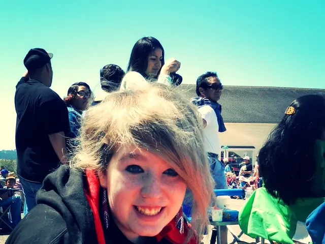 In this image I can see people where few are sitting on chairs and few are standing. Here I can see...