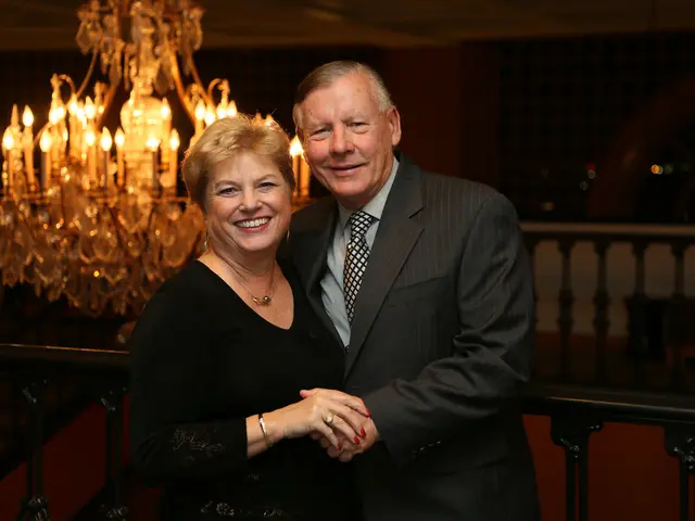 In this picture we can see a man and woman, they both are smiling, behind them we can see a...