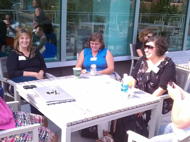 In this image I can see a group of ladies are sitting on the chairs, in the middle there is the...