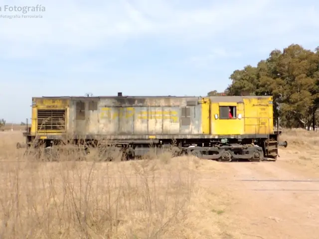 In this picture there is a train and there is a person sitting inside the train. At the back there...