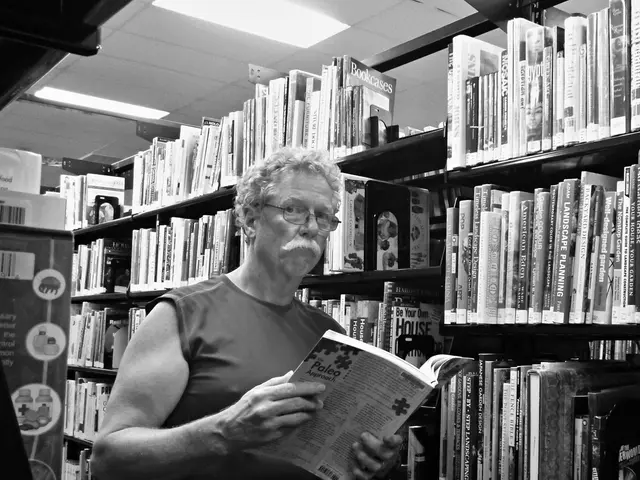 In this picture there is a man standing and holding the book and there are books in the shelf and...