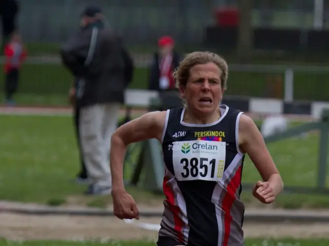 In this image I can see a person running. There is grass and other people at the back.