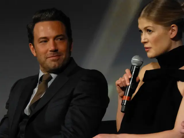 In this picture we can see woman holding mic in her hand and talking beside to her man wore blazer,...