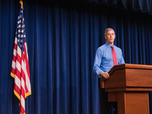 In this image there is a man standing on the stage in front of the podium. On the podium there is a...