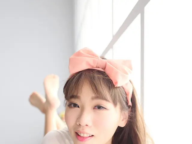 A girl in white t-shirt who is wearing a pink color ribbon on her head is lying on the bench and...