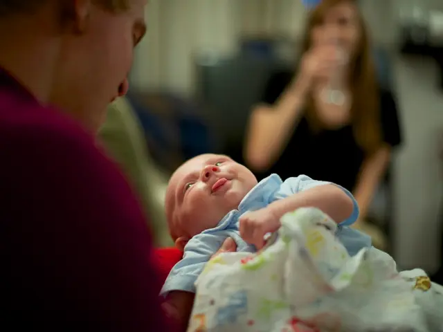 In this image there is a man holding a baby in his hands, in front of him there is women and the...