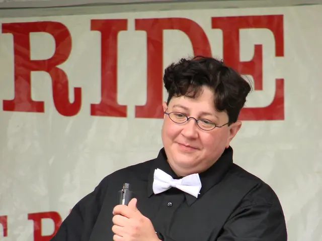 In this image there is a person standing in front of a mic and wearing spectacles, in the...