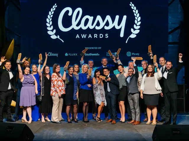 The image shows a group of people standing on top of a stage, smiling and holding awards in their...