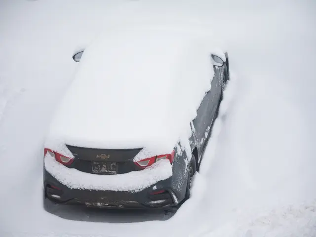 The image shows a car covered in snow on the side of a road. The car is surrounded by a blanket of...