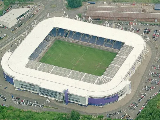 The image shows an aerial view of a soccer stadium in the middle of a city, surrounded by...